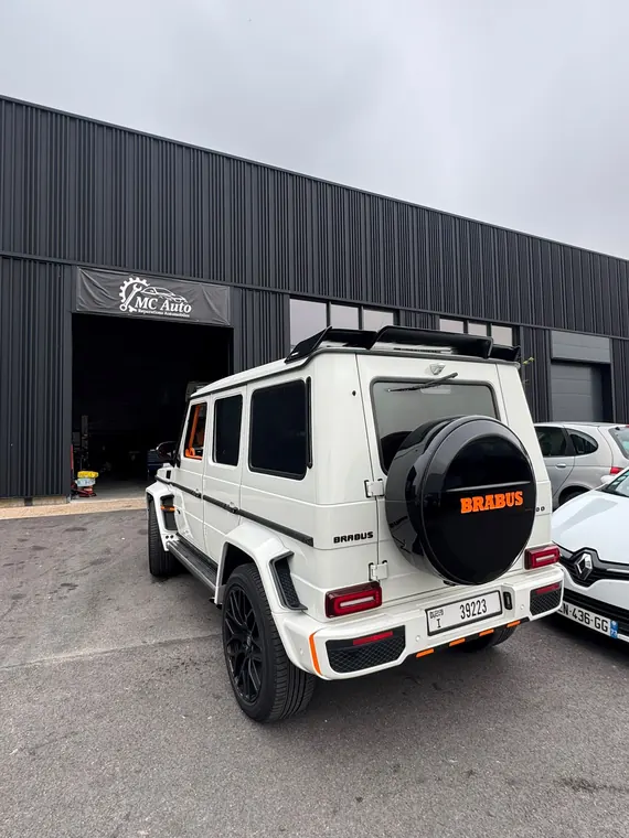 Mercedes Classe G blanche préparée Brabus devant l'enseigne du garage MC Auto